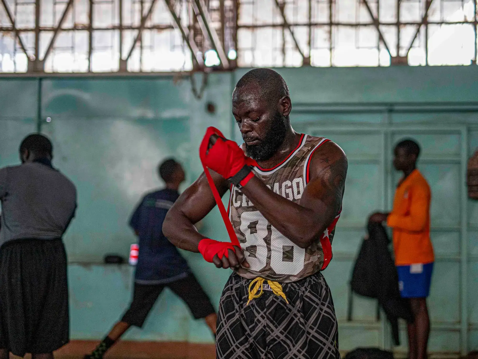 A boxer wraps his hands with red wraps in a busy gym before training.