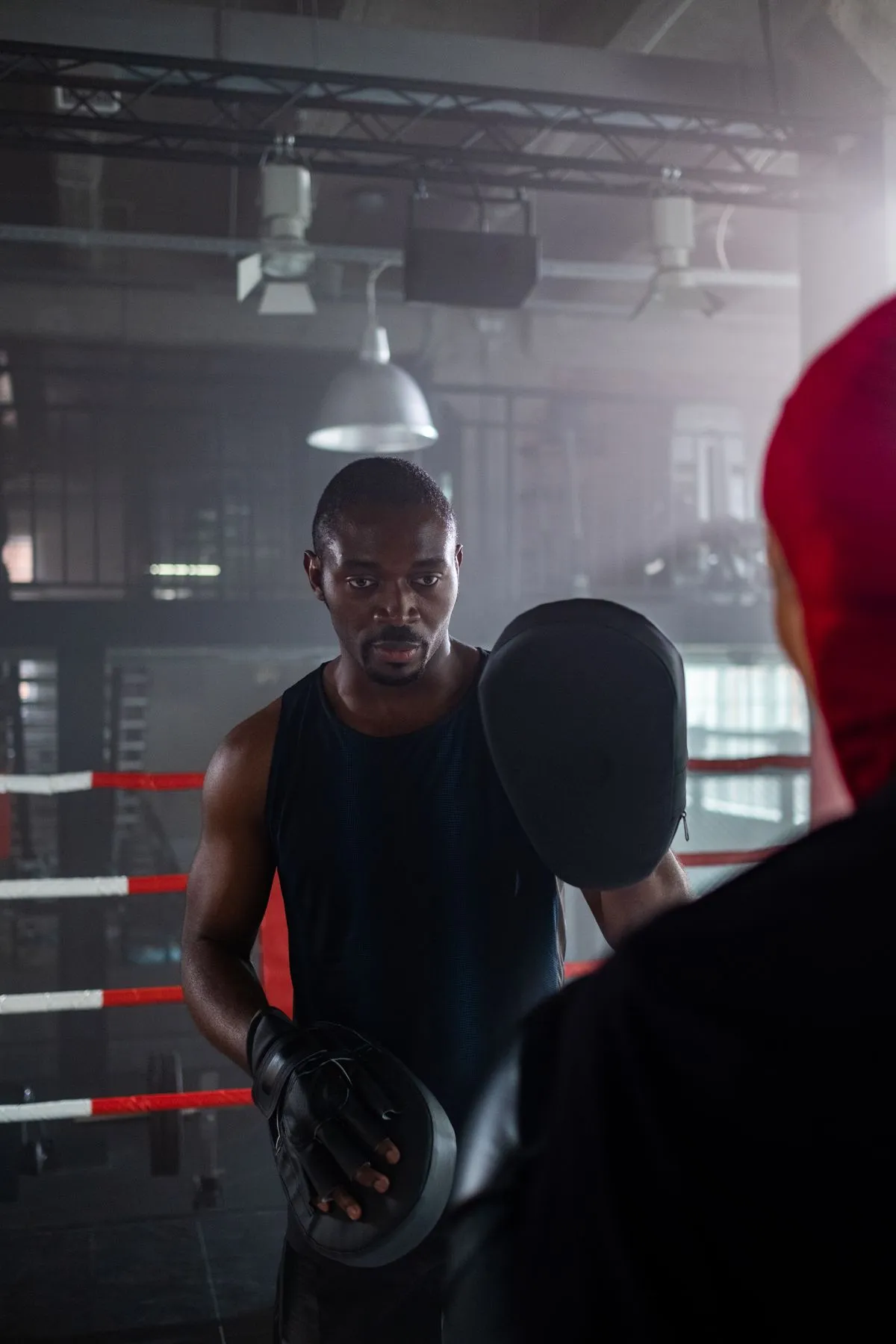 A coach holds focus pads for a boxer inside a ring.