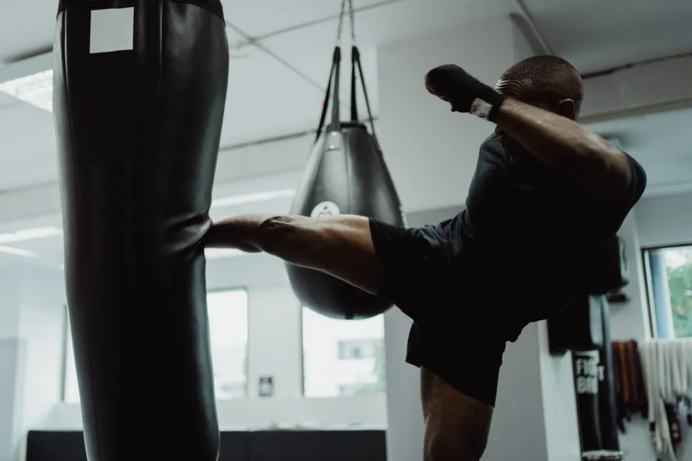 An athlete lands a roundhouse kick on a heavy bag.